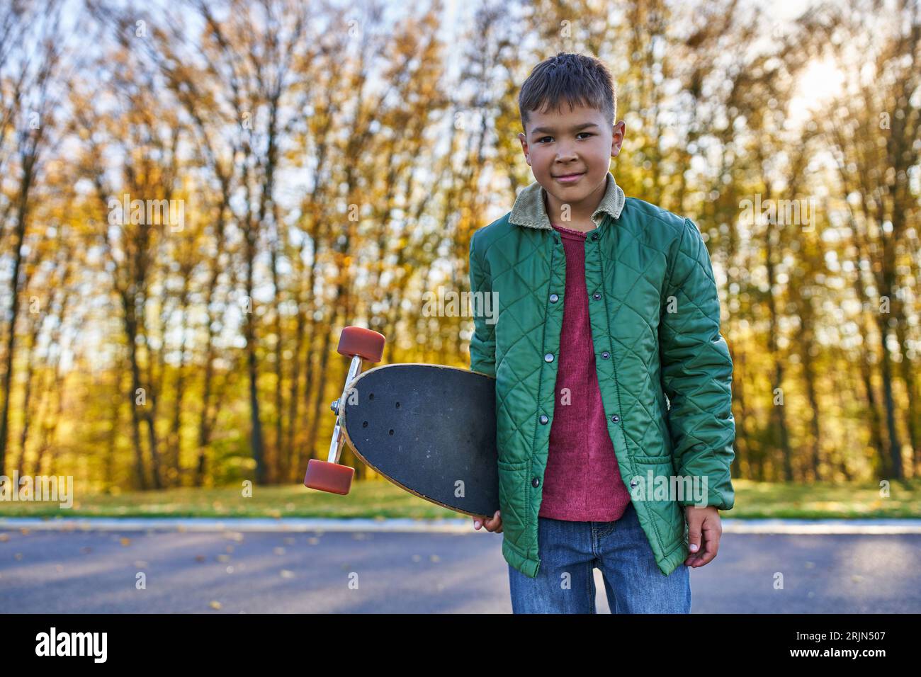 happy african american boy in outerwear holding penny board, autumn park, fall season, portrait Stock Photo
