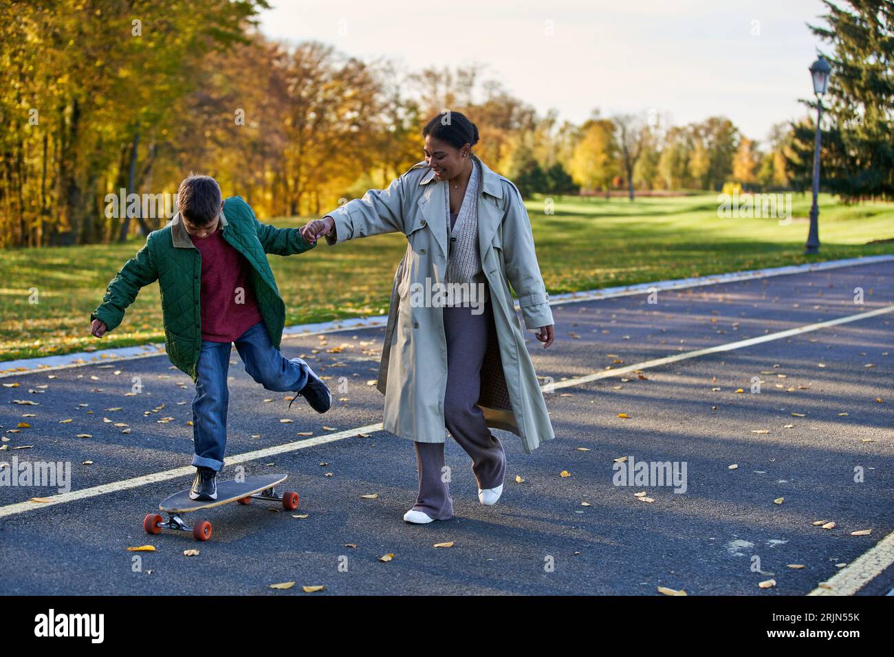 boy riding penny board and holding hands with happy mother, african ...