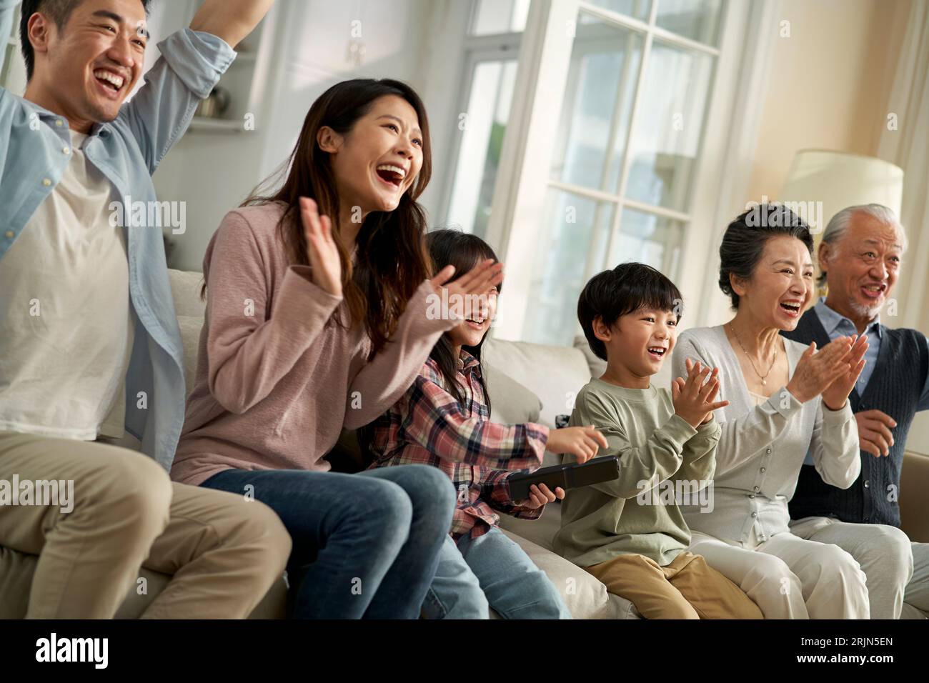 multi generational asian family sitting on couch in living room watching televesion happy and smiling Stock Photo