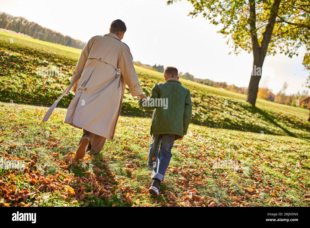 golden hour, mother and son walking in park, hold hands, autumn leaves, fall, african american Stock Photo