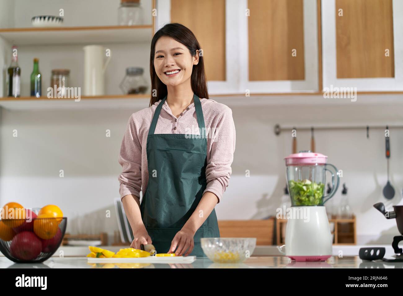 happy young asian woman housewife standing in kitchen looking at camera smiling Stock Photo