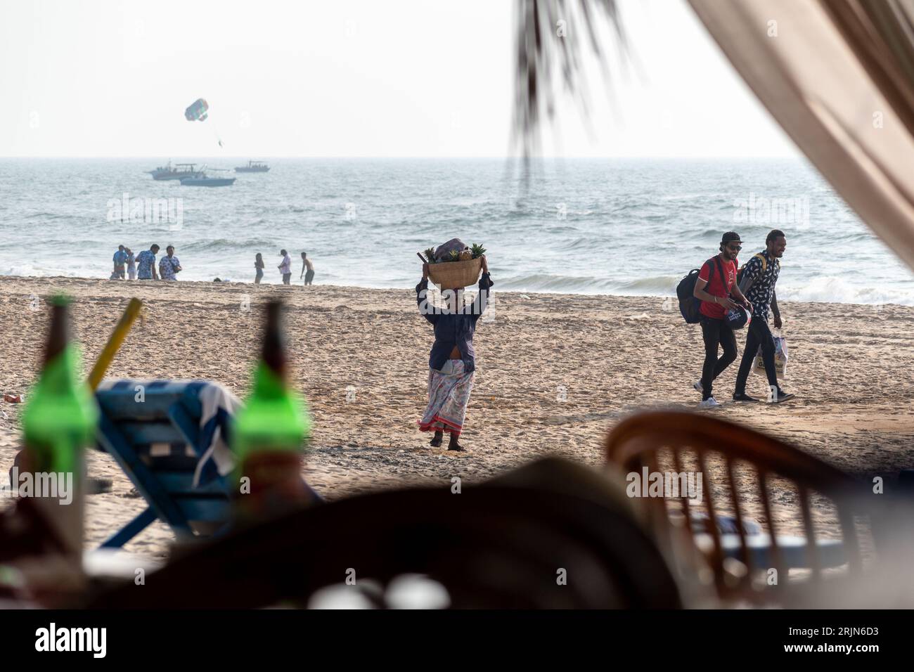 Calangute, Goa, India - January 2023: An Indian female vendor carrying a basket of fruits on her head at a beach in Goa. Stock Photo