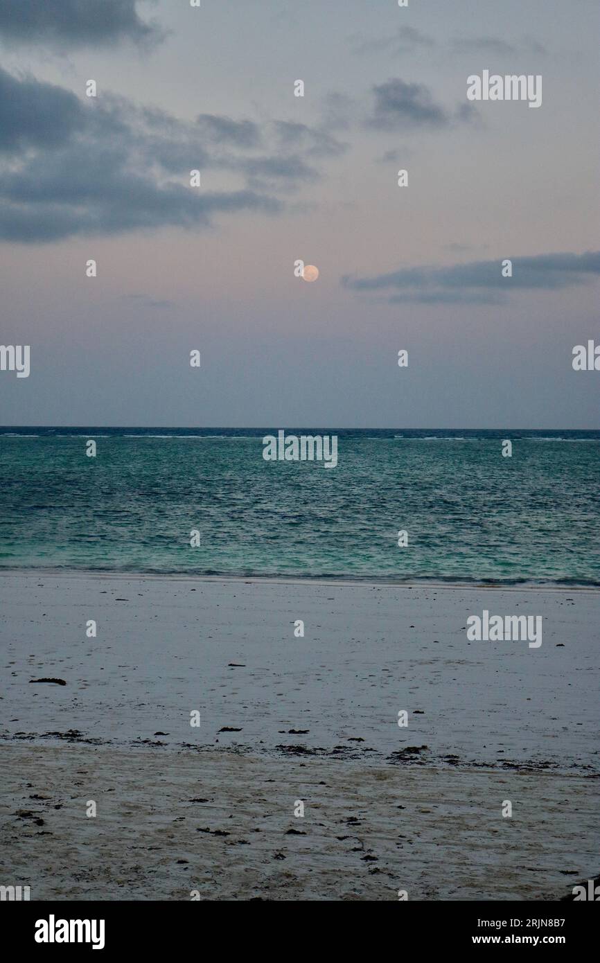 A tranquil seascape of a large, full moon shining brightly against a clear night sky. Stock Photo