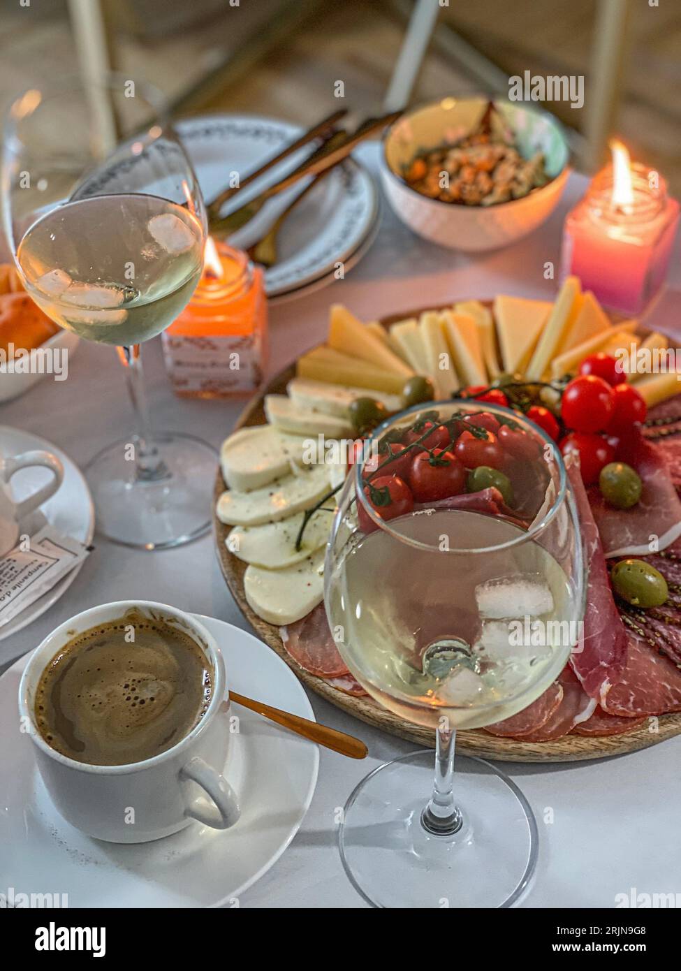 A wooden tabletop with two bottles of white wine and an array of cured meats, cheeses, and crackers Stock Photo