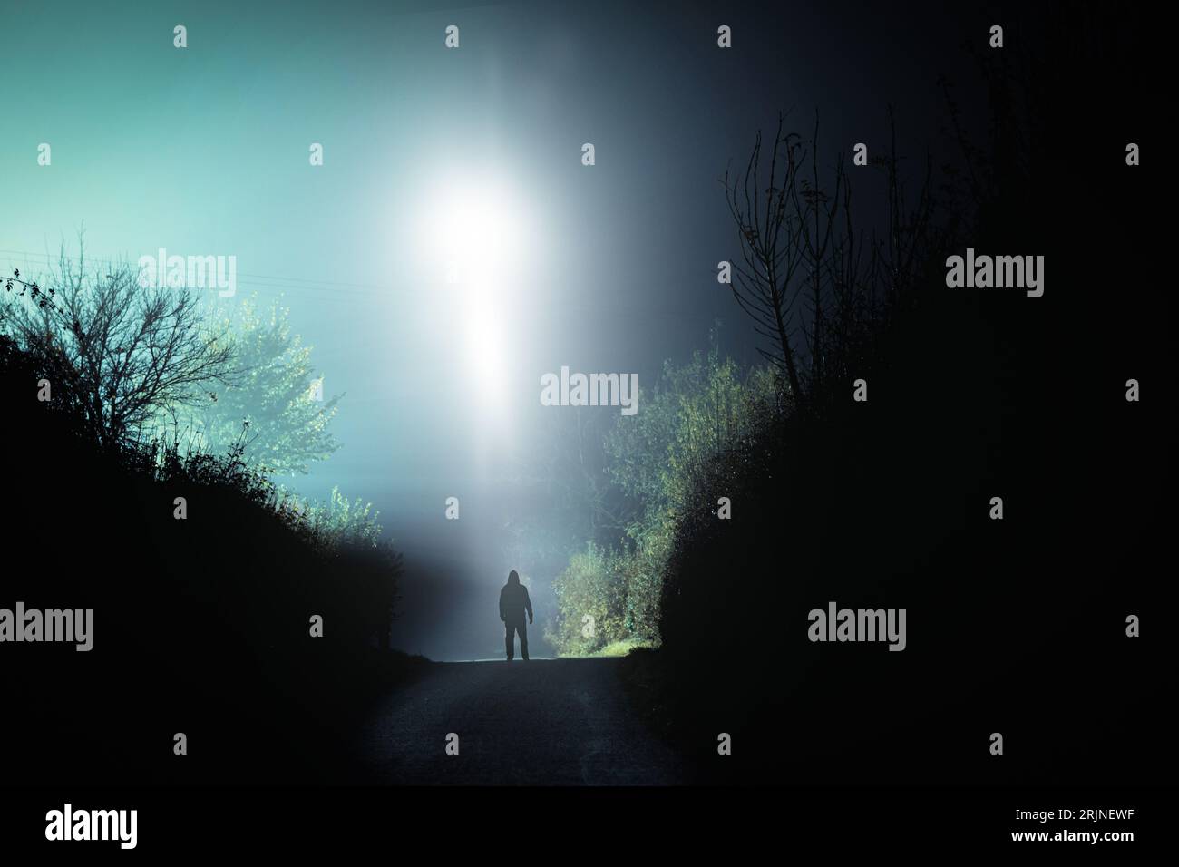A mysterious scary UFO above a hooded figure. On a spooky country road. On a foggy winters night. Stock Photo