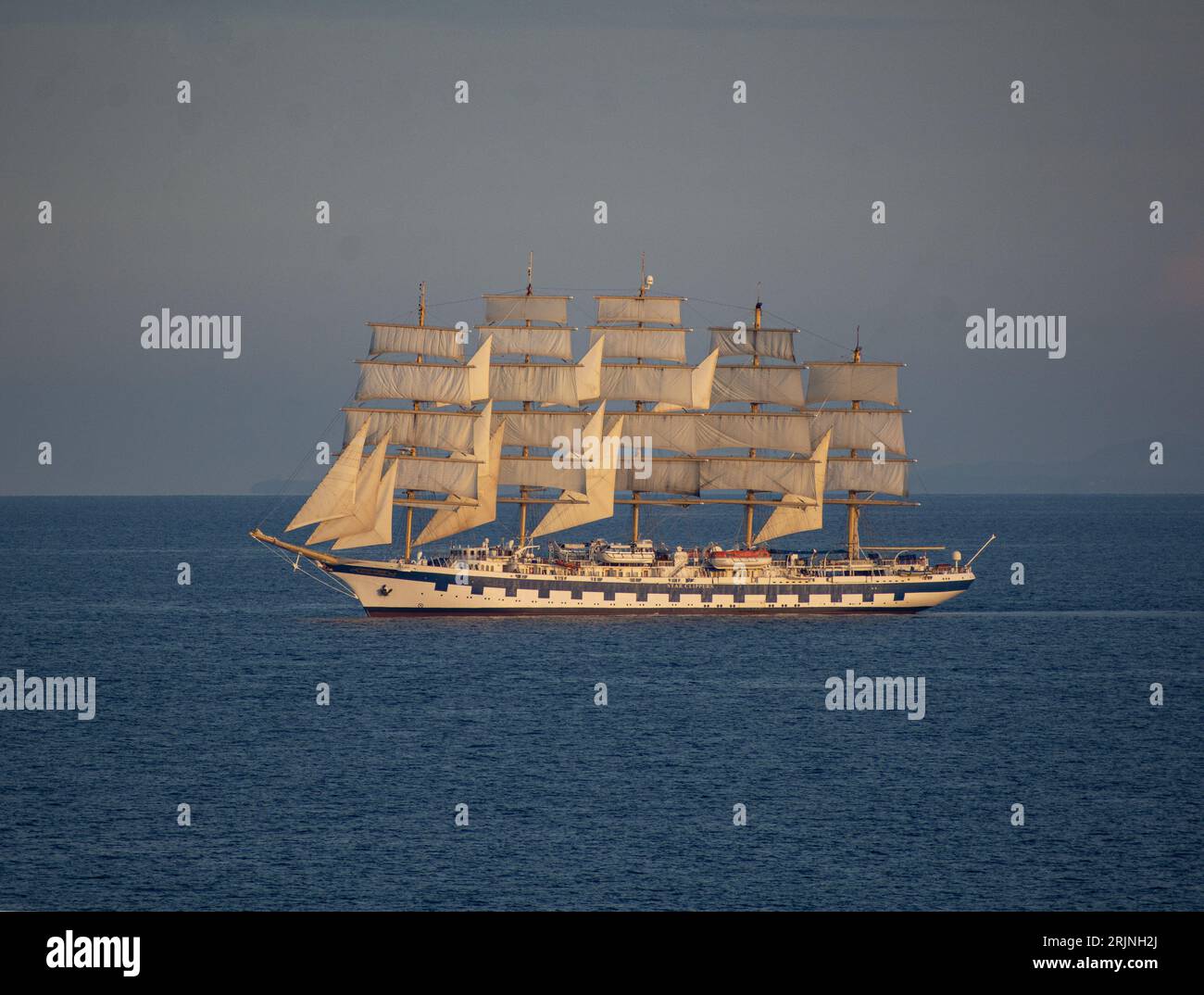 A large sailboat with white sails and blue trim floating in the middle of a vast blue water in Italy Stock Photo