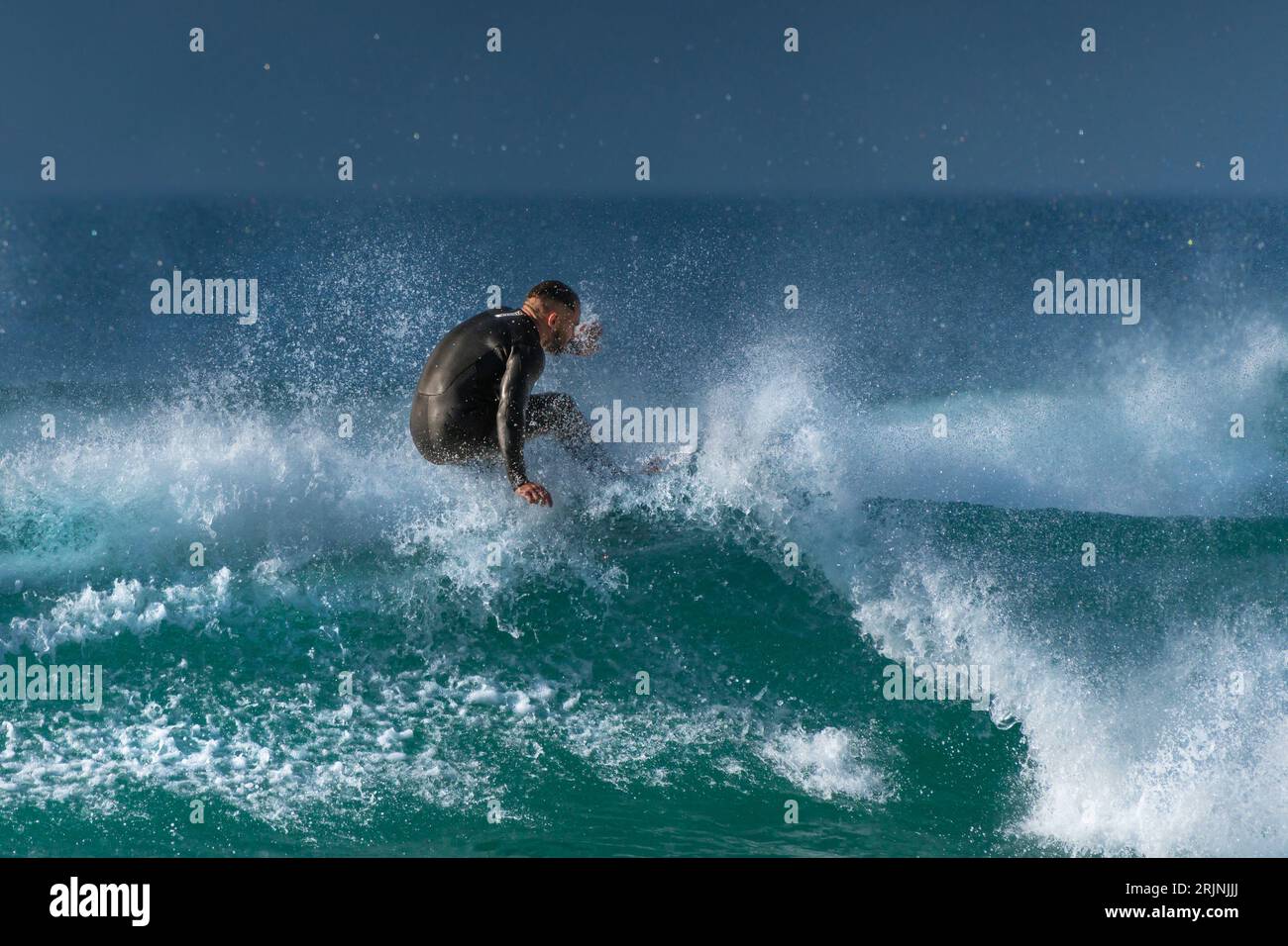 Spectaular surfing action as a male surfer rides a wave at Fistral in Newquay in Cornwall in England in the UK. Stock Photo