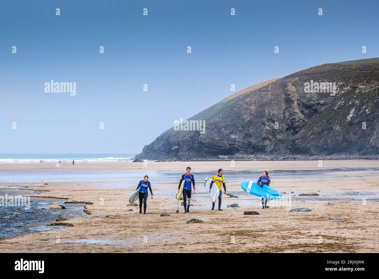 Three novice surfers and their surfing instructor carrying their surfboards after a surfing lesson at Mawgan Porth in Cornwall in the UK. Stock Photo