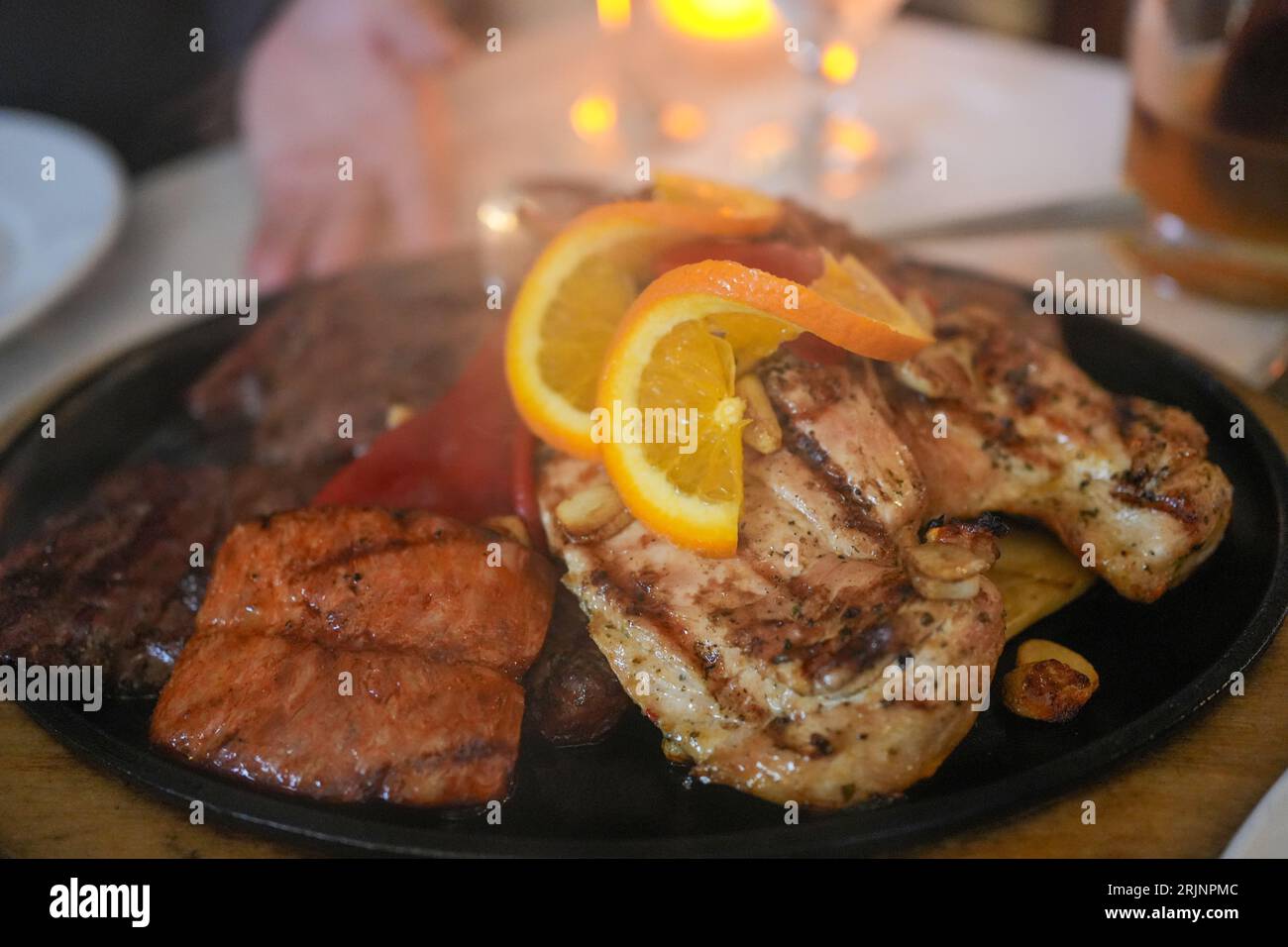 A black plate with a variety of savory meats and slices of orange arranged artfully. Stock Photo