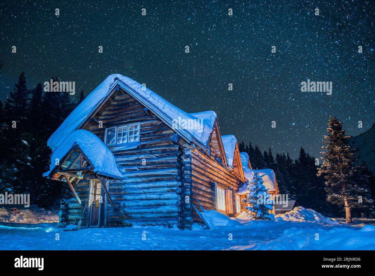 A rustic wooden cabin illuminated against a backdrop of sweeping snow ...