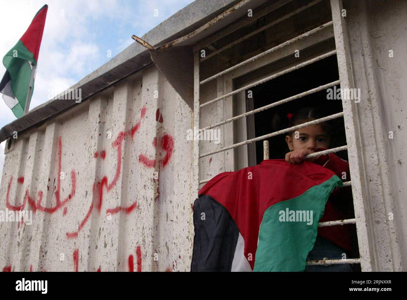 Bildnummer: 51035105  Datum: 21.12.2005  Copyright: imago/Xinhua Palästinensisches Mädchen mit palästinensischer Flagge schaut aus dem Fenster eines Wohncontainers - Protest in Bilin bei Ramallah PUBLICATIONxNOTxINxCHN, Personen; 2005, Ramallah, Bil in, Westjordanland, , , Palästina, Protest, Proteste, Protestaktion, Protestaktionen, Konflikt, Konflikte, Container, Kind, Kinder, Palästinenser, Palästinenserin; , quer, Kbdig, Einzelbild, Israel,  , Gesellschaft, palästinensische Autonomiegebie, Stock Photo