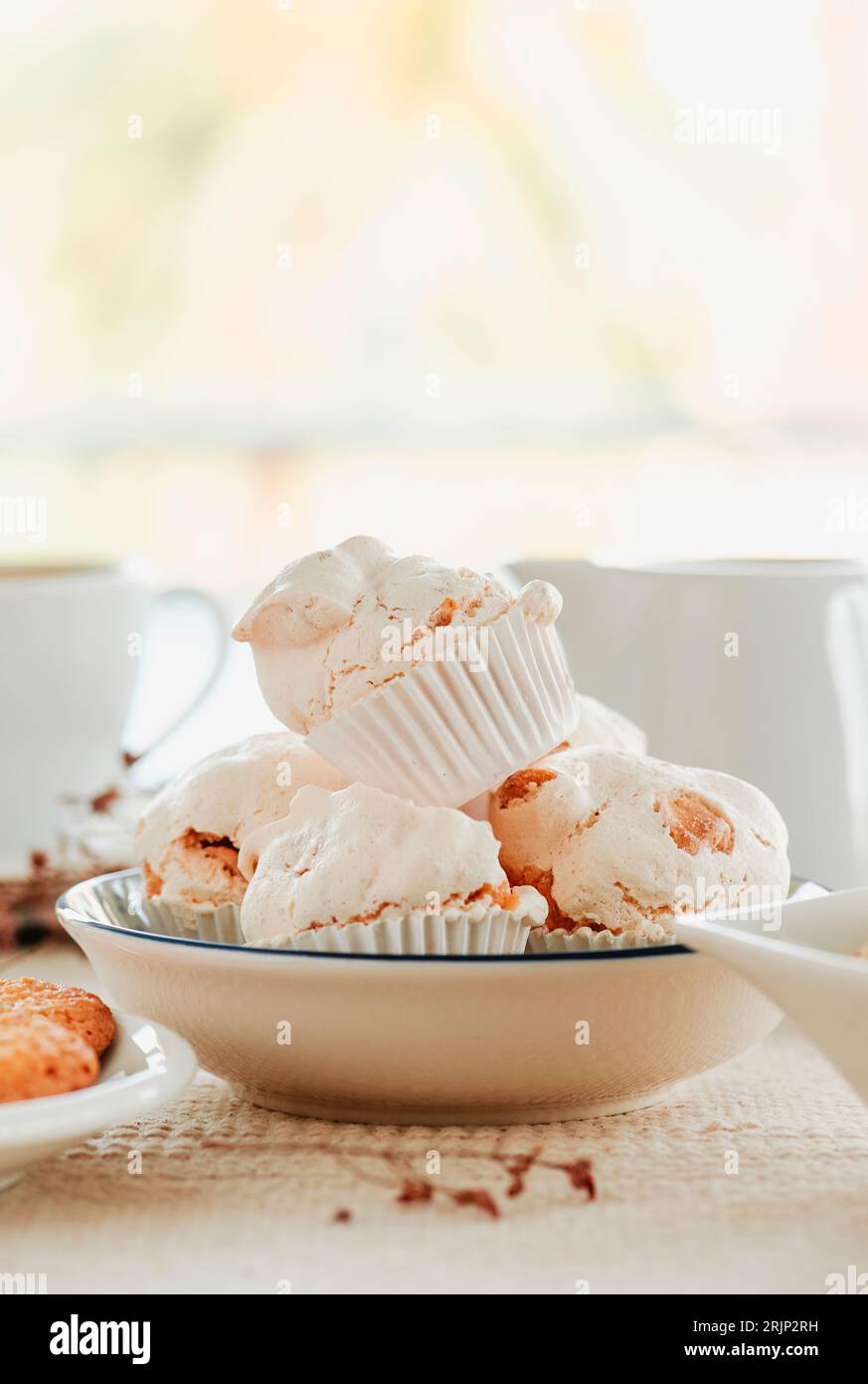 closeup of a white ceramic bowl with some spanish merengues almendrados, baked meringues with almonds, placed on a table next to some ceramic bowls an Stock Photo
