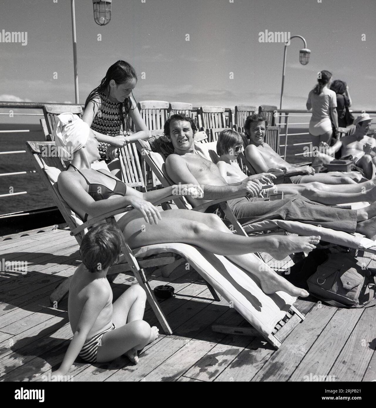 circa late 1960s, early 70s... historical, a family in swimsuits relaxing in deckchairs outside on the deck of the cruise ship, MS Sagafjord, a luxury ocean-liner of the era. Launched in 1965 as a trans-atlantic cruise ship, after various changes of ownership including sailing under the Cunard flag, and being renamed the Saga Rose in 1997, she was scrapped in 2010, when new safety measures meant the need for extensive upgrades. Stock Photo