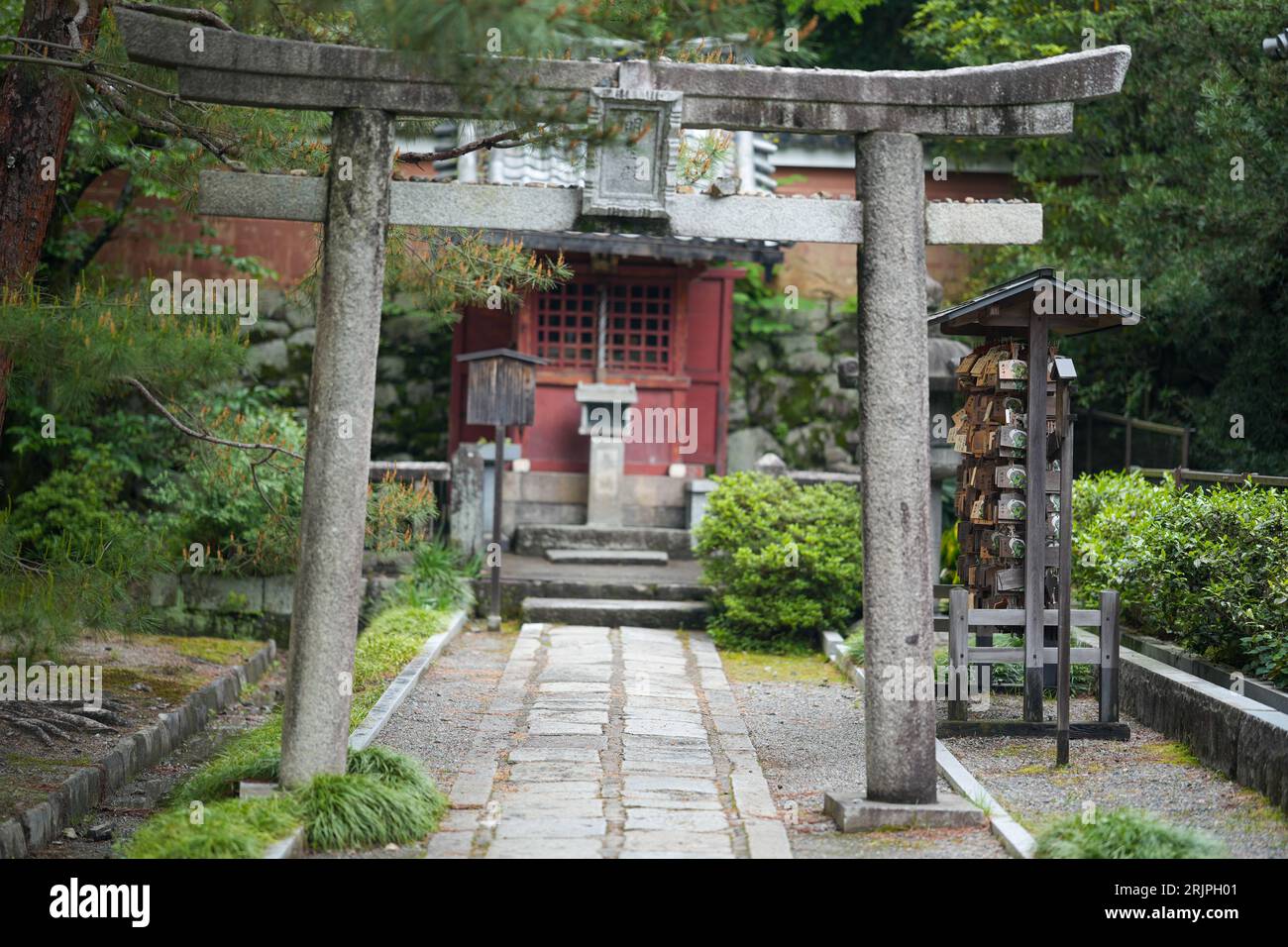 A stone pathway with a stone arch leading to a red building in a park ...