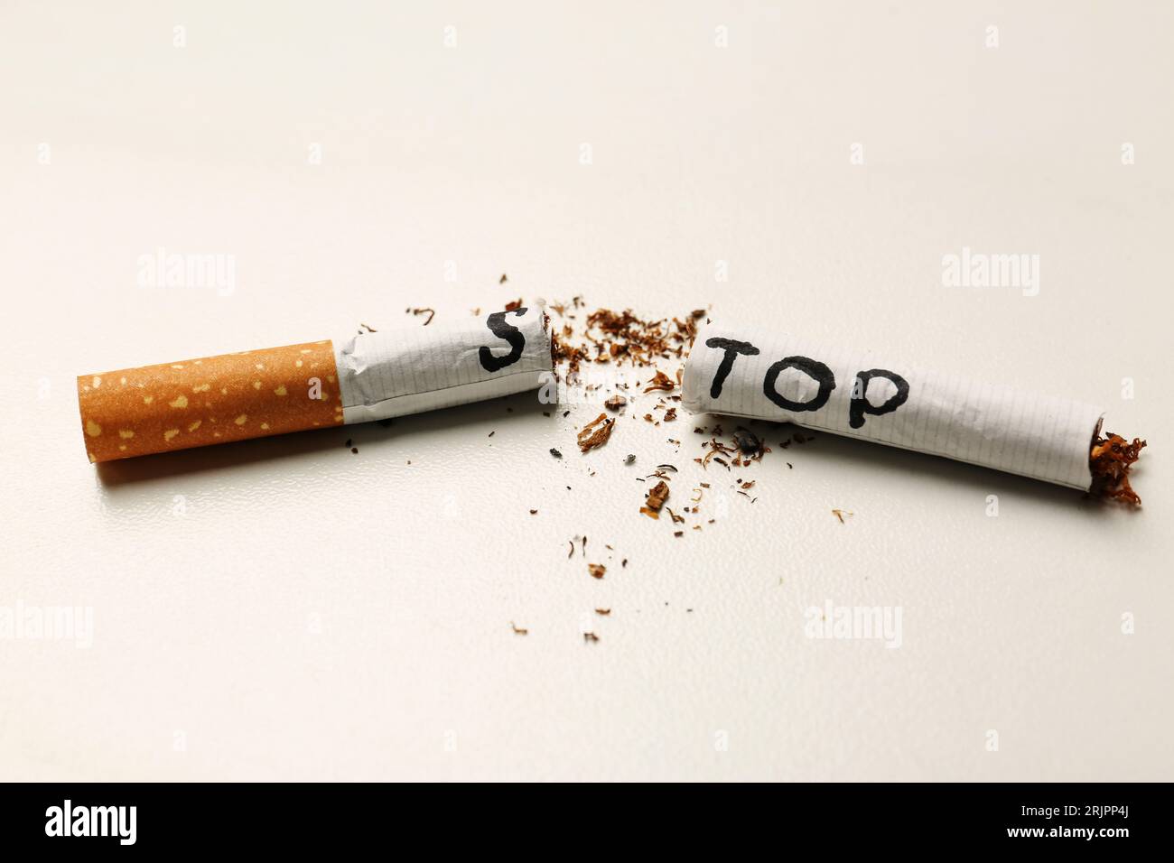 Word Stop written on cut cigarette on white table, closeup. No smoking  concept Stock Photo