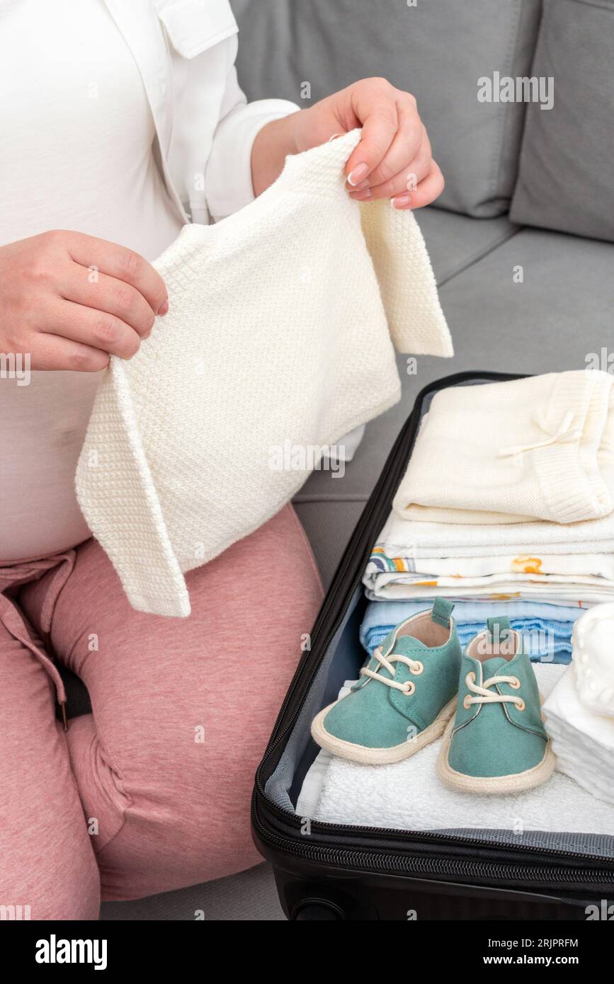 Pregnant woman diligently packing suitcase at home, preparing