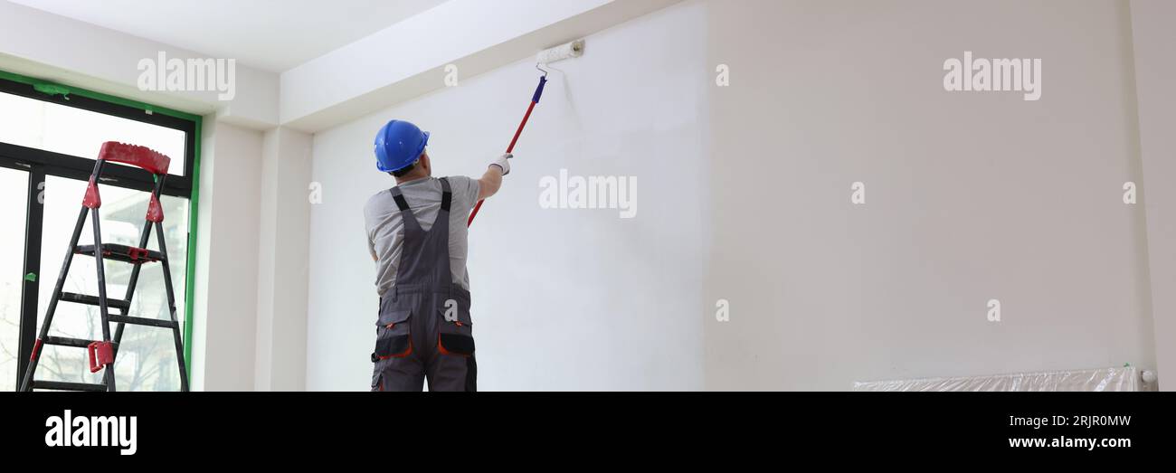 Professional painter paints office wall with roller brush. Stock Photo
