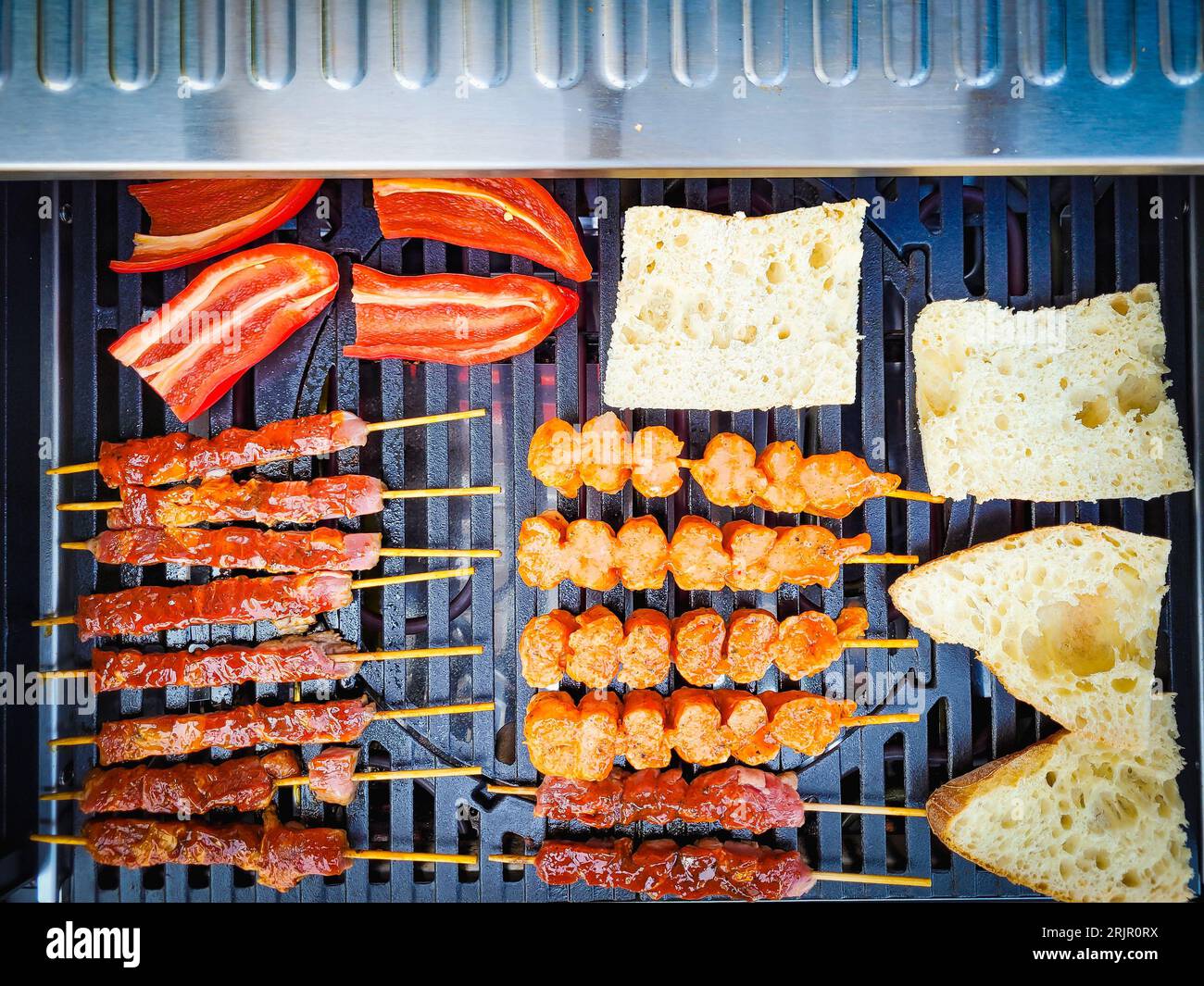 An overhead view of a grill with raw meat, bread pieces and red peppers placed on it Stock Photo