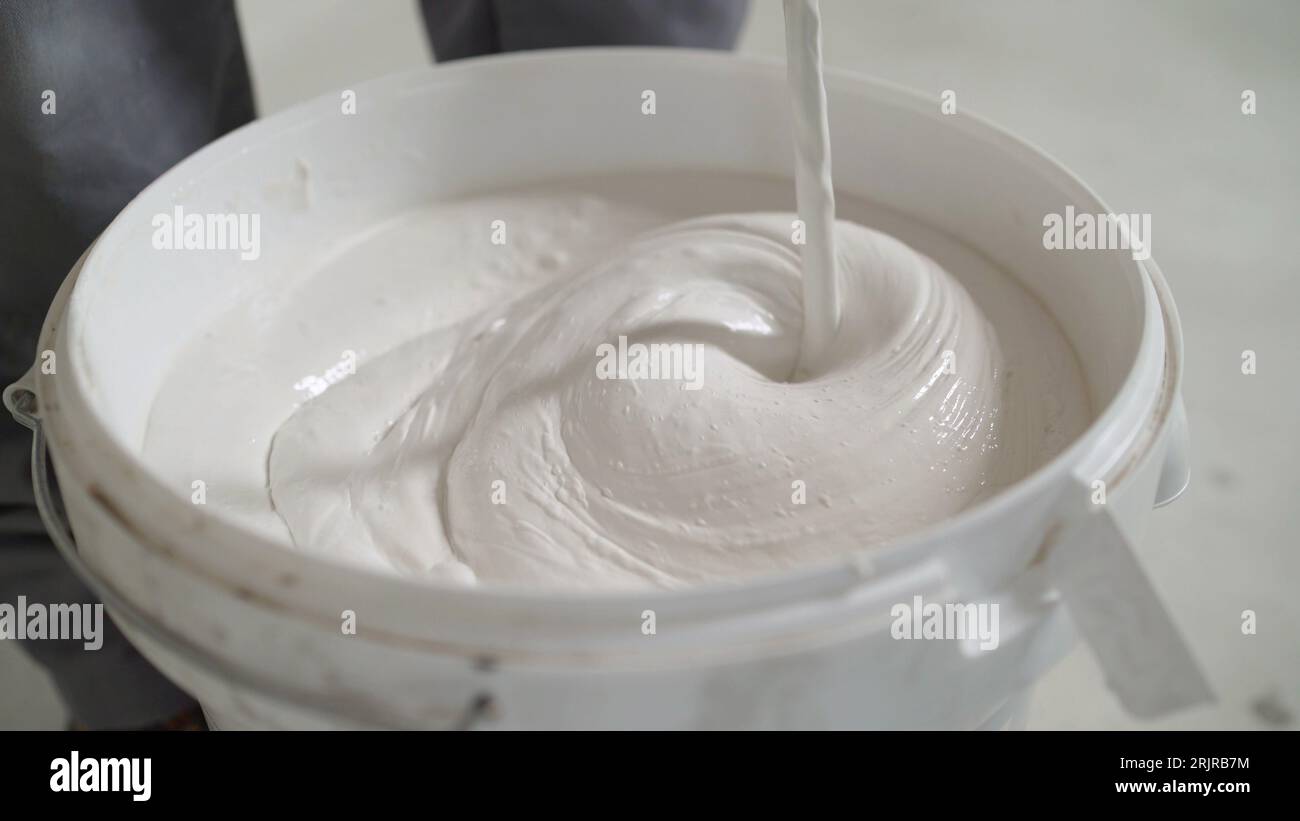 Mixing mortar in a white bucket. A worker mixes mortar for white tiles