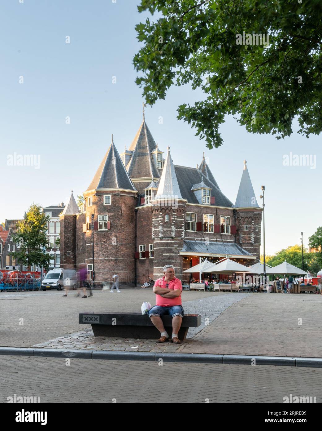 A man sits on a bench outside The Waag restaurant and cafe in Nieuwmarkt Square in the center of Amsterdam. Stock Photo