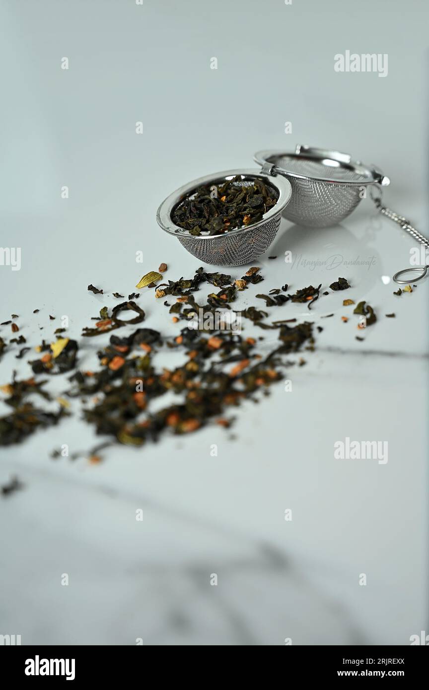 A vertical closeup of a tea ball strainer filled with tea leaves on a white marble table Stock Photo