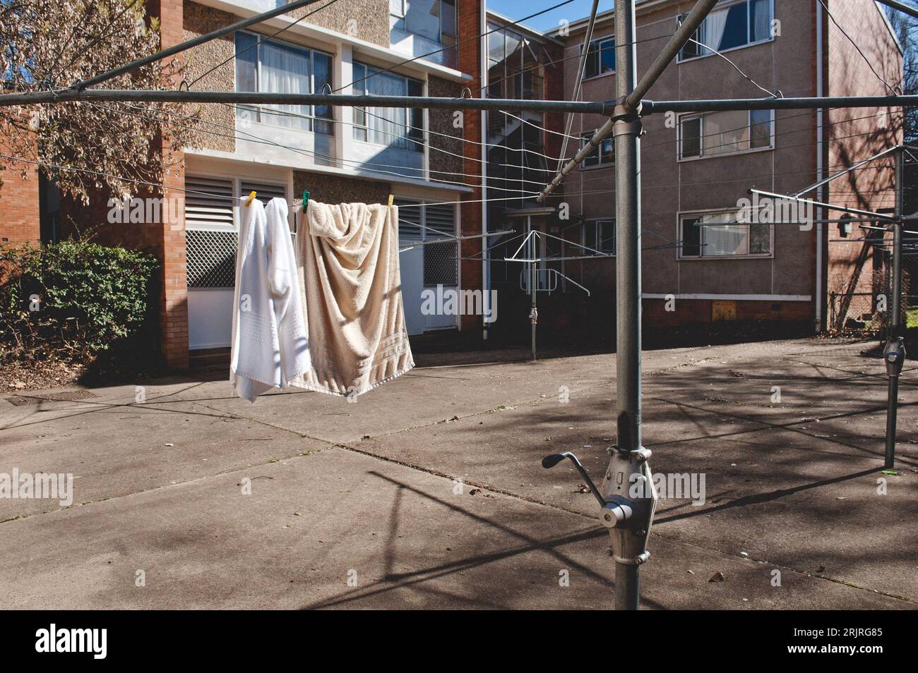A vintage metal Hills Hoist clothesline stands outside a weathered apartment building Stock Photo