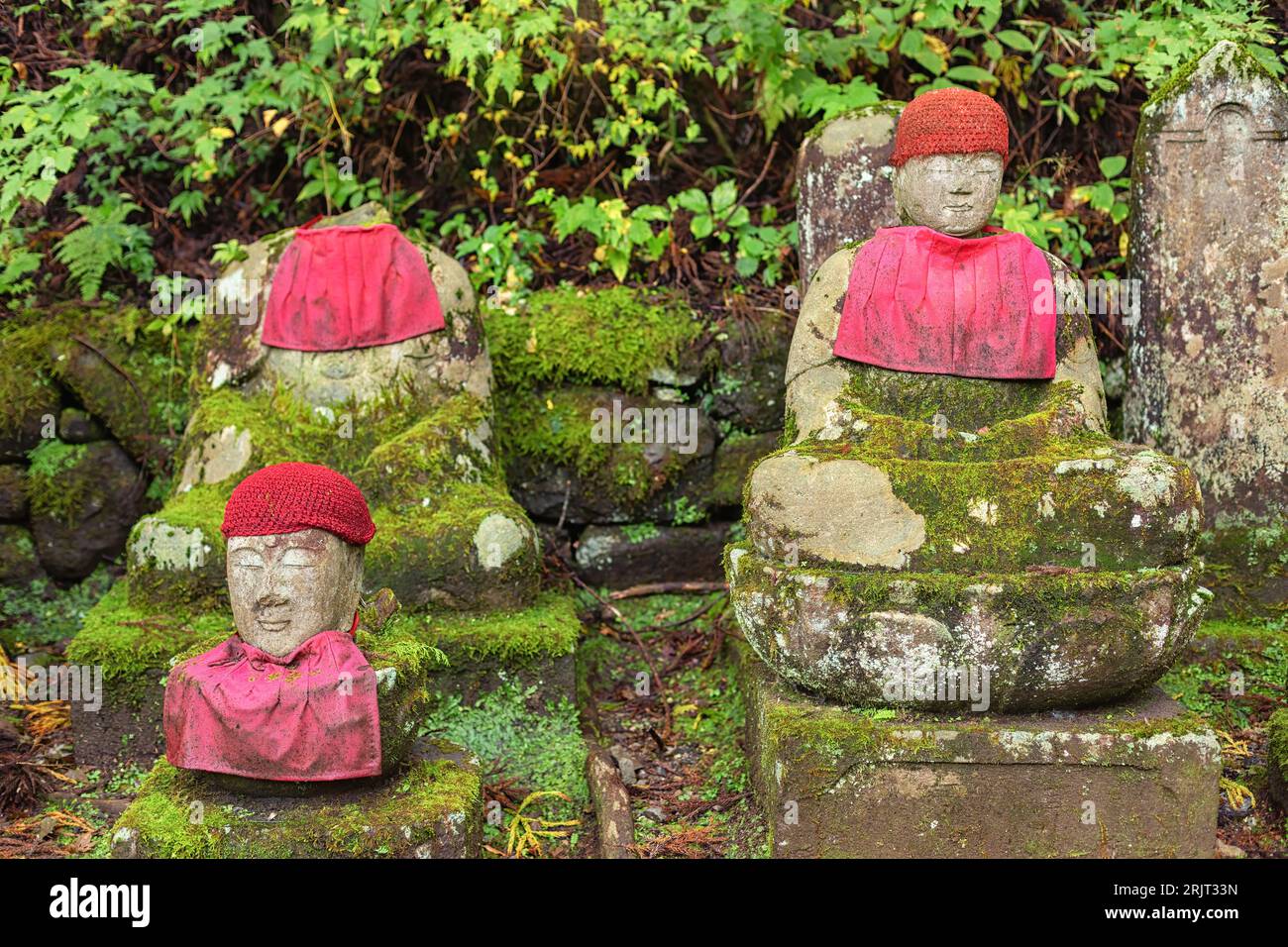Moss covered Jizo statues, one decapitated,, wearing red hats and bibs