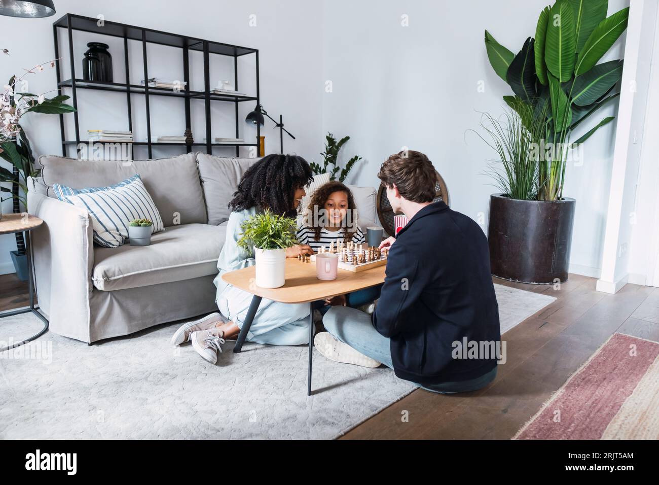 Parents sitting in livingroom teaching daughter to play chess Stock Photo