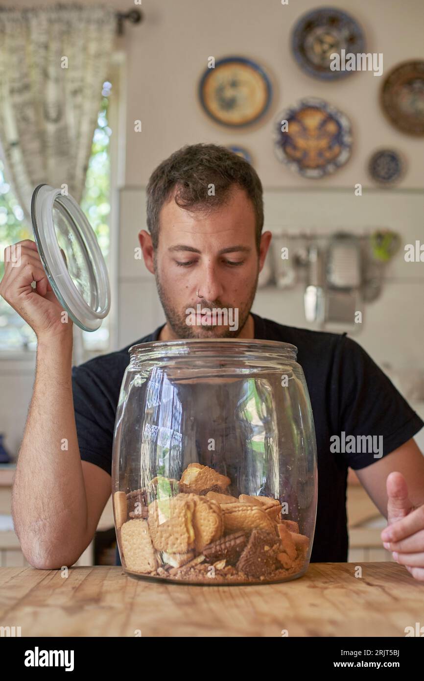Man sitting in kitchen, looking in cookie jar Stock Photo Alamy
