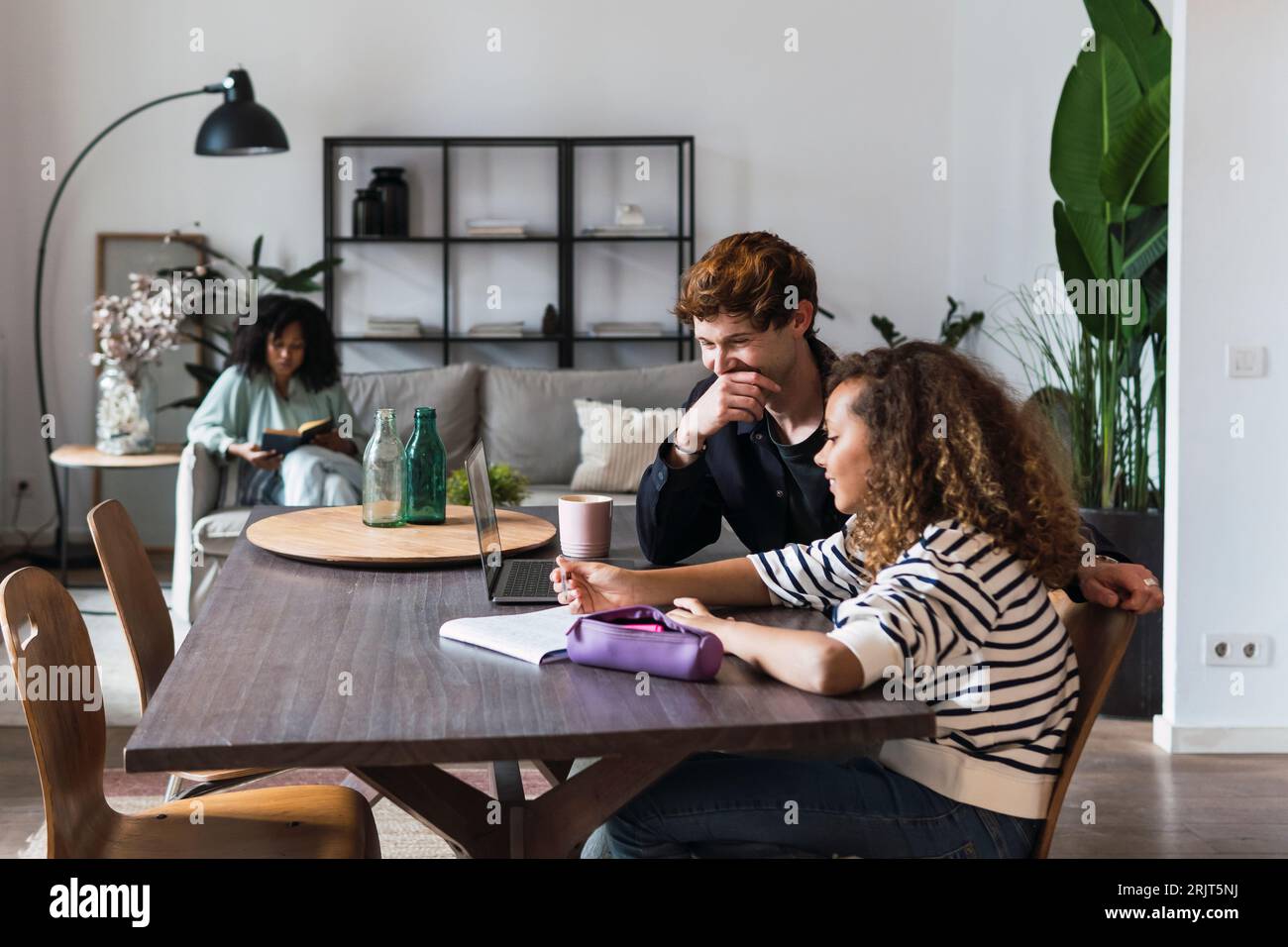 Father watching daughter doing homework with mother reading in ...