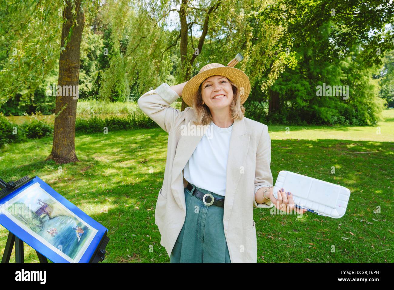Happy Mature Woman Wearing Hat Standing By Painting In Park Stock Photo happy-mature-woman-wearing-hat-standing-by-painting-in-park-stock-photo