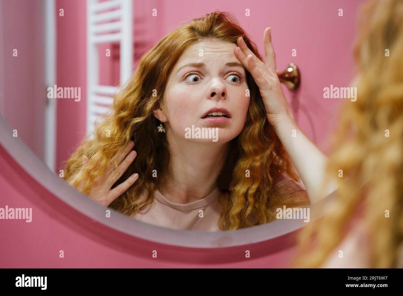 Worried woman examining face looking in mirror at home Stock Photo