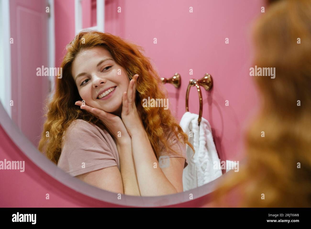 Reflection of young woman touching face in bathroom mirror Stock Photo