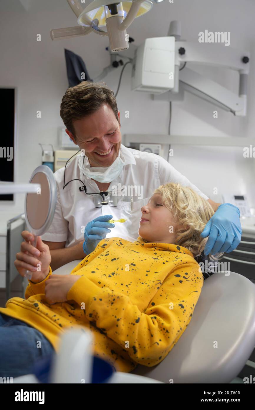 Blond boy looking in hand mirror at dental clinic Stock Photo