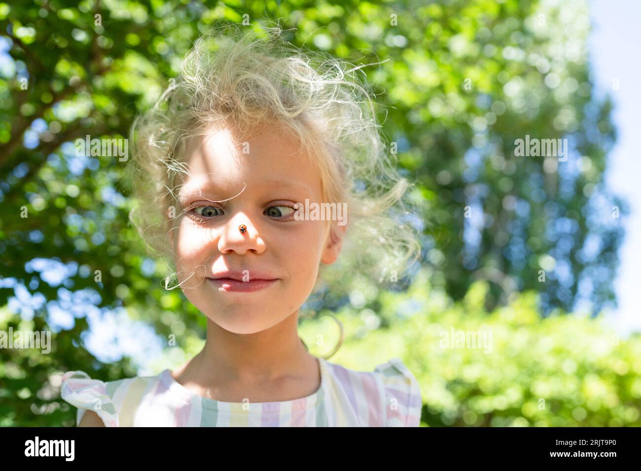 Smiling girl with ladybug on nose in park Stock Photo