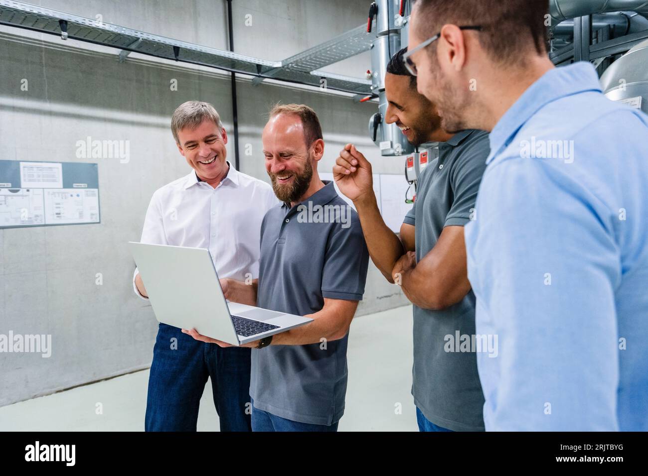 Happy businessmen and employees with laptop having a meeting in factory Stock Photo