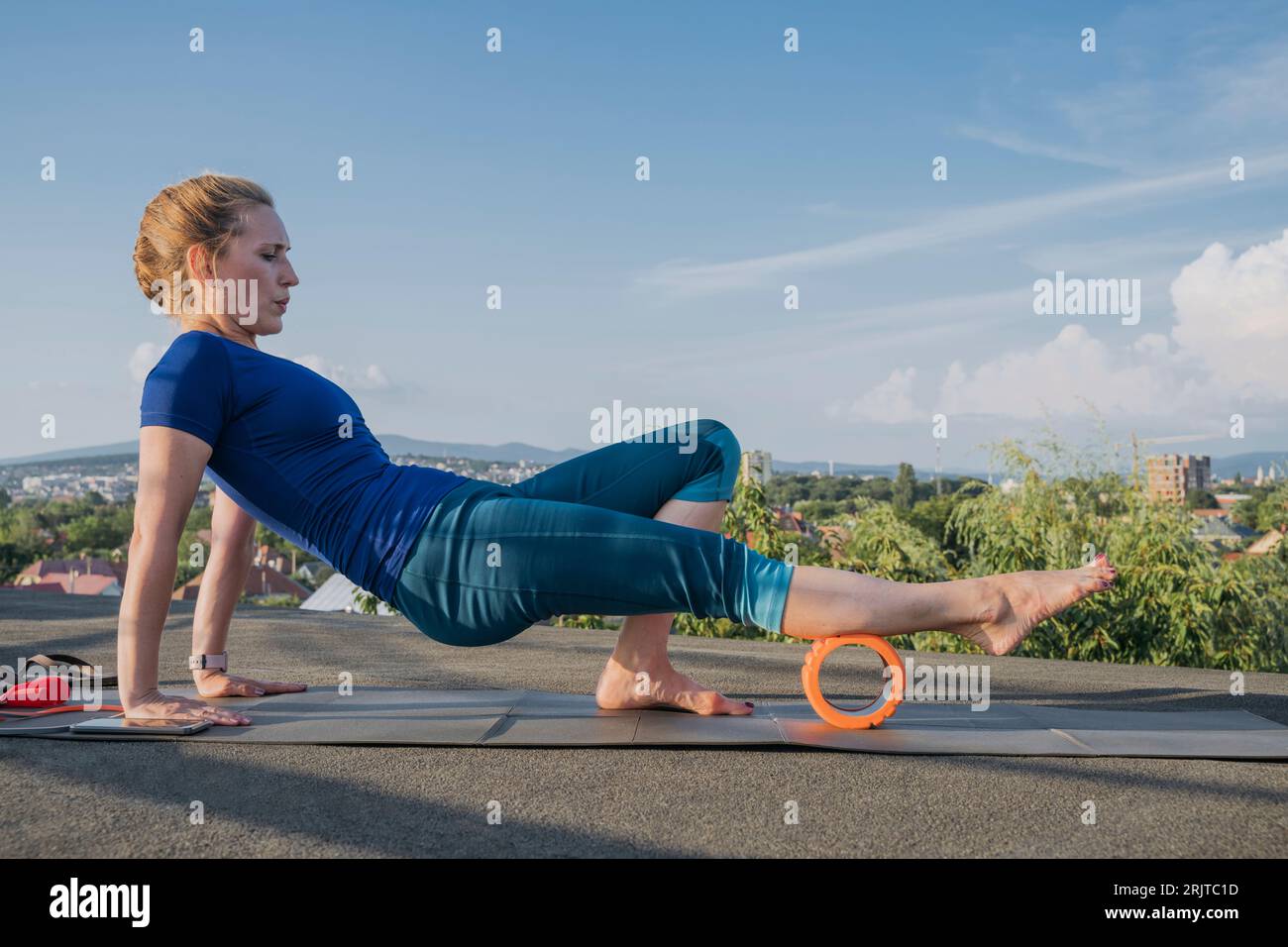 Blond woman exercising with foam roller on rooftop Stock Photo - Alamy