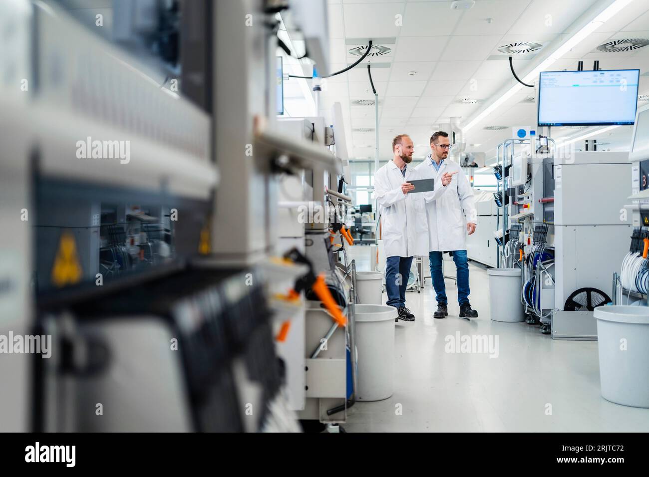 Discussing technicians walking through electronics factory holding digital tablet Stock Photo