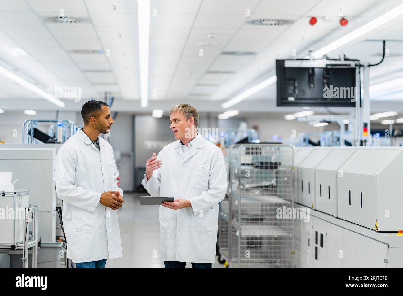 Two electrical technicians walking through factory workshop discussing over digital tablet Stock Photo