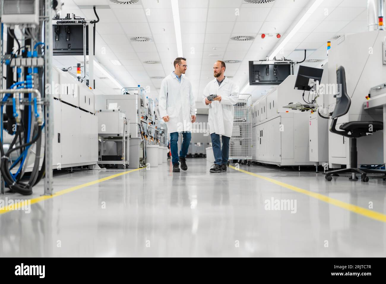 Discussing technicians walking through electronics factory holding digital tablet Stock Photo