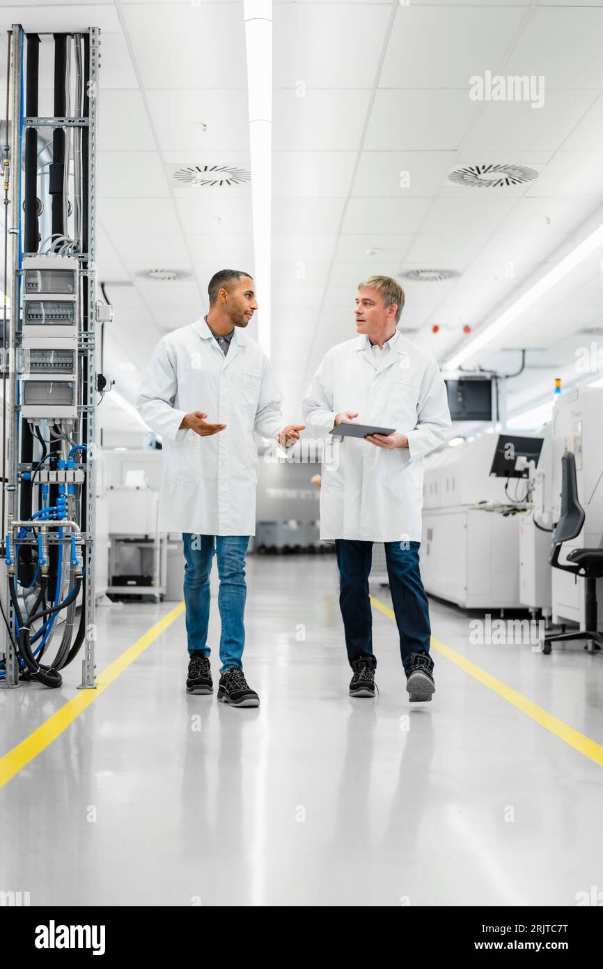 Discussing technicians walking through electronics factory holding digital tablet Stock Photo