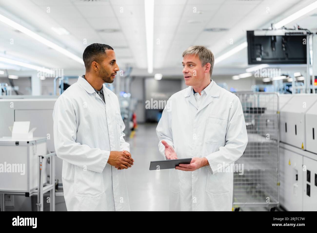 Discussing technicians walking through electronics factory holding digital tablet Stock Photo
