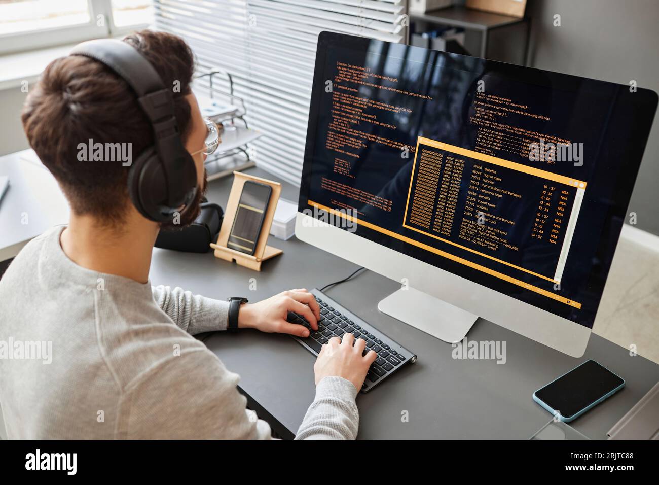 Young computer programmer wearing wireless headphones coding on computer Stock Photo
