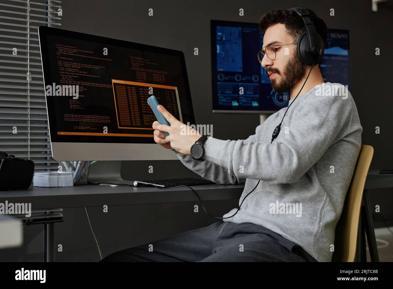 Young computer programmer using smart phone at desk Stock Photo