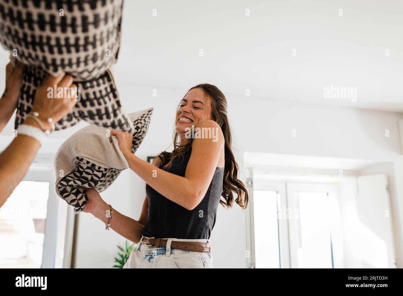 Happy young woman having pillow fight with friend in apartment Stock Photo