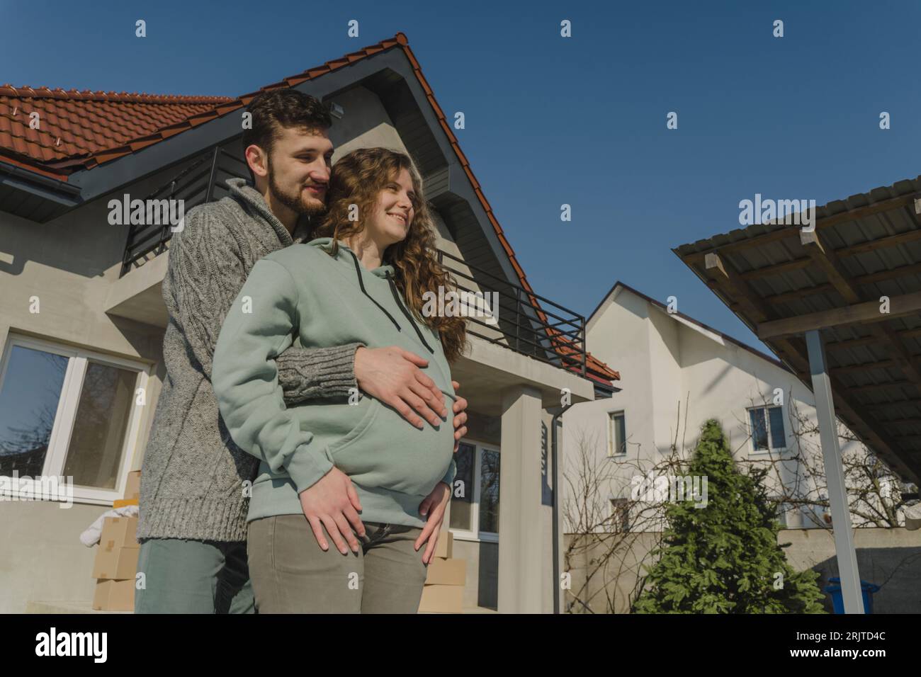 Smiling man embracing pregnant woman outside house Stock Photo - Alamy