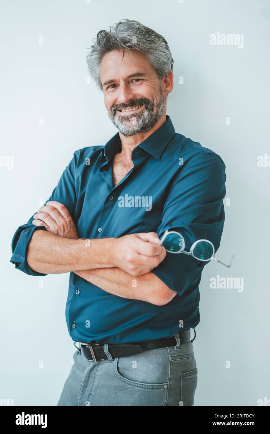 Confident businessman standing with arms crossed in front of wall Stock ...
