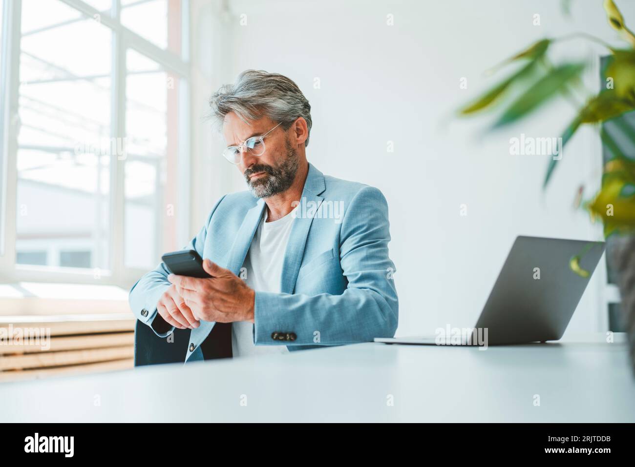 Businessman using smart phone sitting at office Stock Photo