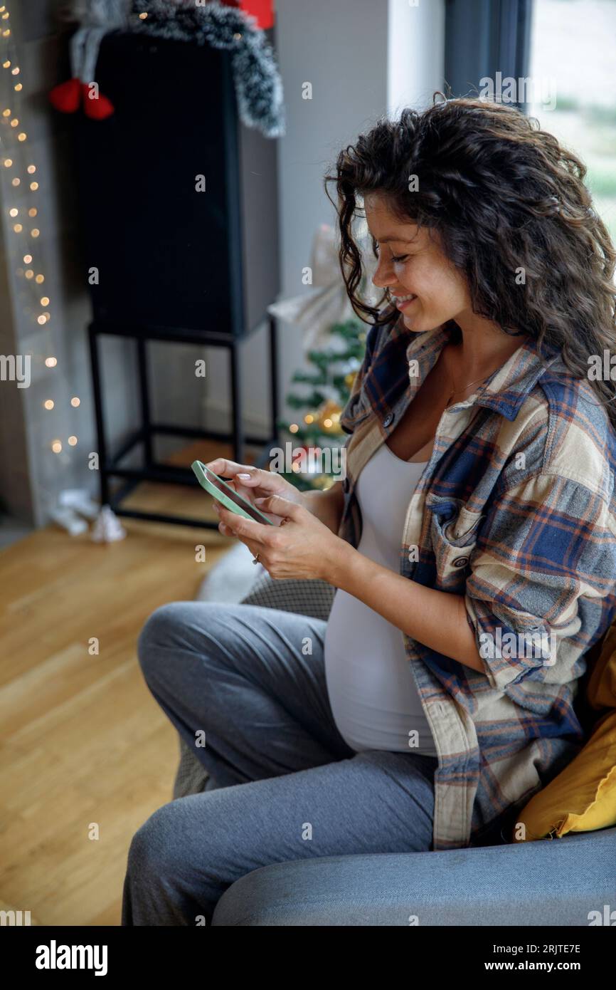 Happy expectant mother using smart phone at home Stock Photo