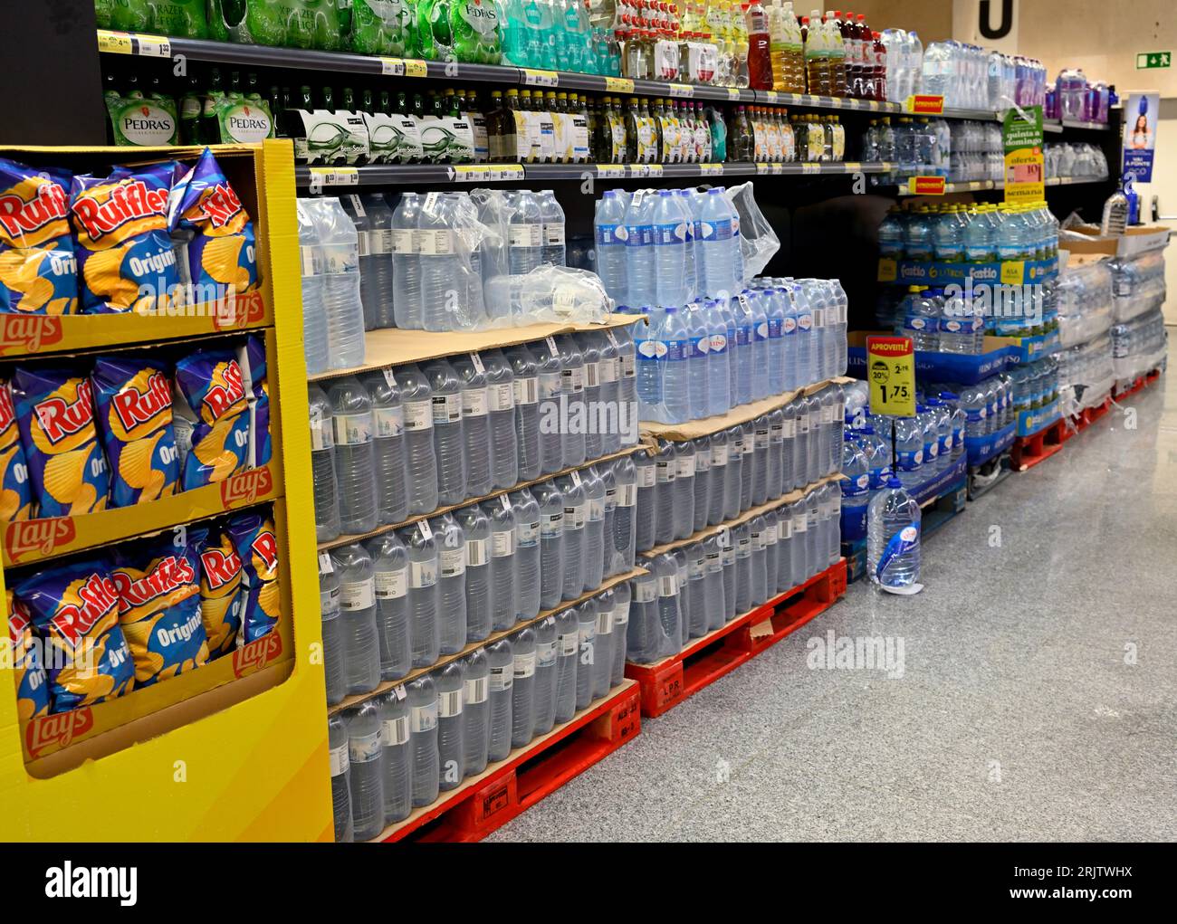 Inside hypermarket Pingo Doce aisle with stack of bottled water, other drinks and snacks, Stock Photo